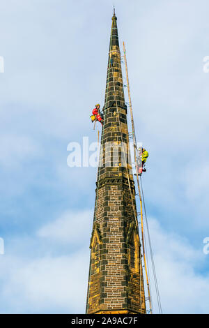 Steeplejack on church spire in Southport, Merseyside. UK Weather: 14th Nov, 2019.  Cold, cloudy conditions with a stiff breeze for steeplejacks carrying out urgent repairs to Holy Trinity Church Steeple in the town centre. Sunny conditions with a light breeze are expected to continue to allow maintenance, storm damage repair and restoration work to continue. Holy Trinity Church, on Manchester Road, was placed in category B of the At Risk register, meaning there is an “immediate risk of further rapid deterioration, loss of structural integrity with the condition of the church branded “poor”. Stock Photo