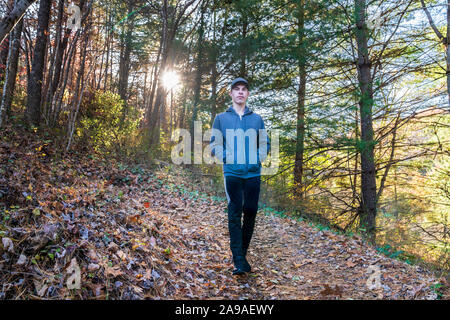 Hiking outdoors: Young man walking down a mountain trail in autumn leaves with a sun star behind him. Stock Photo
