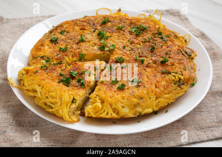 Homemade spaghetti omelette on a white plate, side view. Close-up.