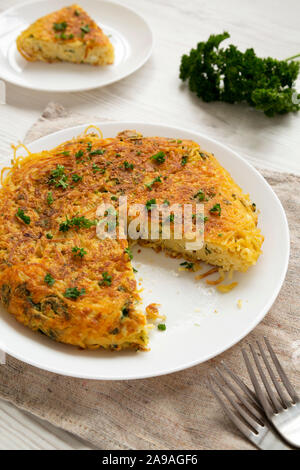 Homemade spaghetti omelette on a white plate, low angle view. Closeup.