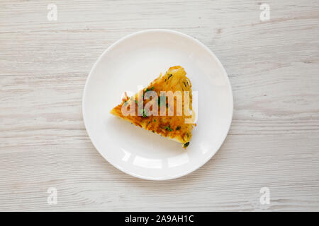 A piece of spaghetti omelette on a white plate on a white wooden background, overhead view. Flat lay, top view, from above. A piece of spaghetti omelette on a white plate on a white wooden background, overhead view. Flat lay, top view, from above.