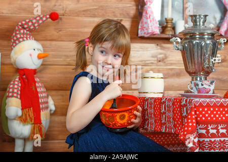 Girl Masha cooks porridge in a pot. On the table is a samovar and toys. Stock Photo