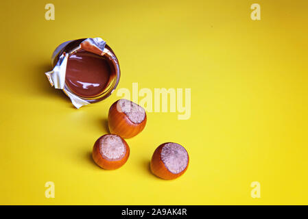 Three unpeeled hazelnuts and a jar of chocolate paste on a yellow background. Flatley. Stock Photo