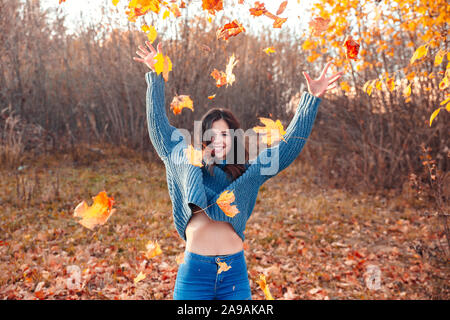 Young happy woman playing with dry maple leaves in park Stock Photo