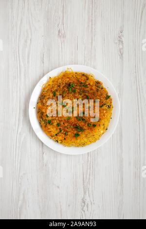 Homemade spaghetti omelette on a white plate over white wooden background, top view. Flat lay, overhead, from above.