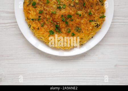 Homemade spaghetti omelette on a white plate over white wooden surface, top view. Space for text.