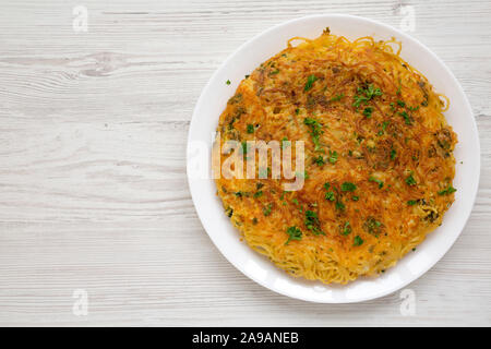 Homemade spaghetti omelette on a white plate over white wooden background, top view. Copy space.