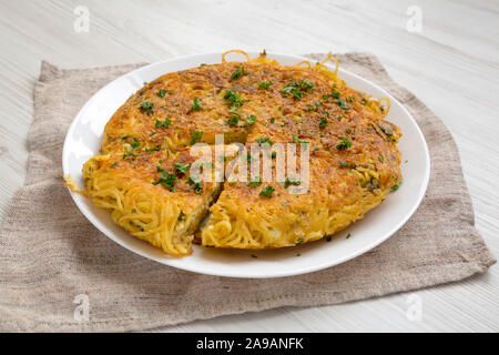Homemade spaghetti omelette on a white plate, side view. Close-up.