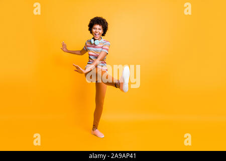 Full length body size photo of cheerful cute nice girlfriend throwing her leg ahead dancing grimacing behaving like a child wearing striped t-shirt Stock Photo