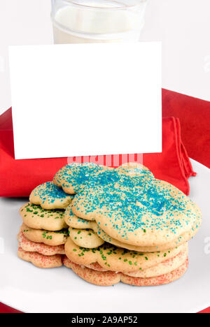 A stack of homemade holiday sugar cookies with sprinkles on each one. There is a blank note to Santa Claus and a glass of milk. Stock Photo