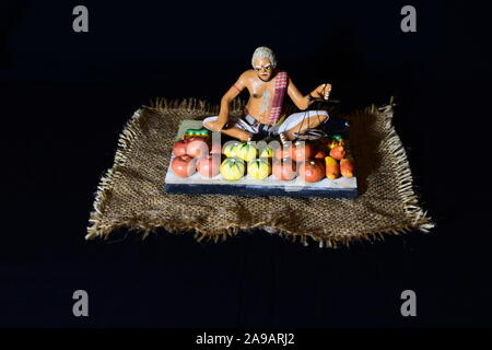 Hand made clay figurine of a vegetable vendor on black background. Stock Photo