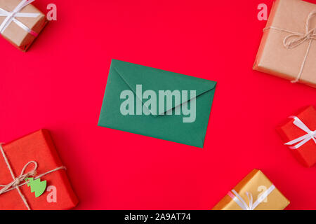 Top above high angle view photo of green envelope lying among wrapped boxed isolated over vibrant color red background Stock Photo