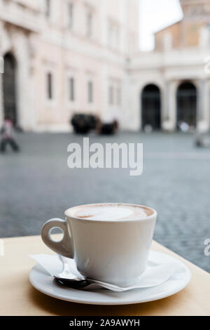 closeup of a cappuccino served in a white ceramic cup, on a table in an outdoors terrace of a cafe in Rome, Italy Stock Photo