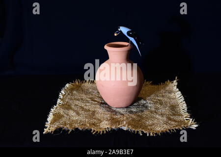 A clay pitcher with a clay crow perched on its rim on a piece of sackcloth. Stock Photo