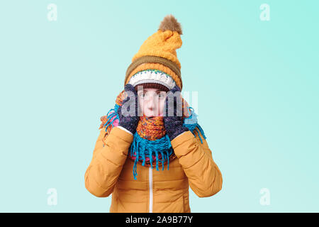 Caucasian shocked funny woman in several hats and scarfs being surprised on blue background. Winter fashion. Stock Photo