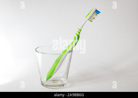Close-up of a new and clean toothbrush in a transparent and empty glass on a light gray background. Concept photo of dental care and personal hygiene. Stock Photo