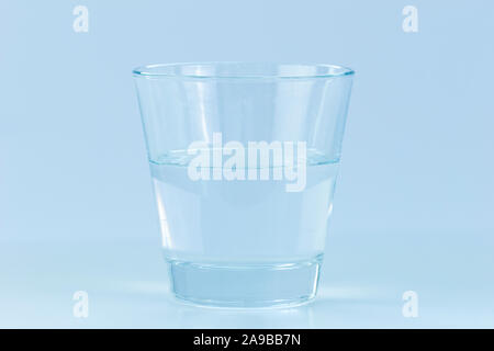 Close-up of a transparent drinking glass half full or empty of water. Concept photo of positive or negative attitude. Blue hue. Stock Photo