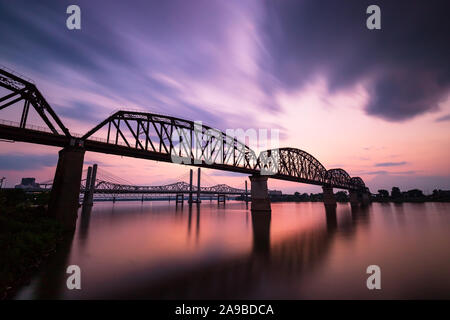 Long exposure of the Big Four Bridge in Louisville, KY with a sunset of clouds moving and water silky smooth. Stock Photo