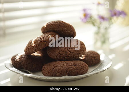 Oatmeal cookies in a plate close-up on a background of blinds and a bouquet of flowers Stock Photo