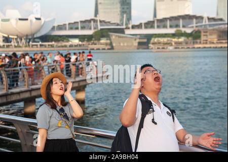 18.07.2019, Singapore, , Singapore - Tourists posing on the banks of the Singapore River for photos with the Marina Bay Sands Hotel in the background. Stock Photo