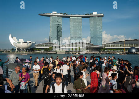 19.07.2019, Singapore, , Singapore - Tourists in Merlion Park on the banks of the Singapore River with the Marina Bay Sands Hotel in the background. 0 Stock Photo
