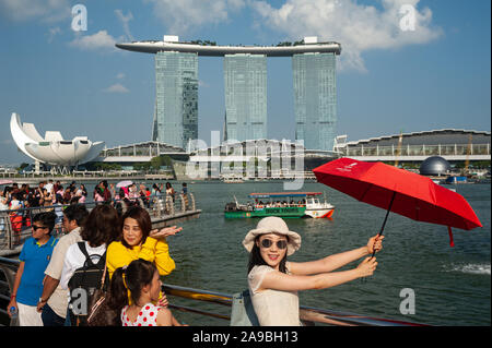 01.08.2019, Singapore, , Singapore - Tourists posing in Merlion Park on the banks of the Singapore River for photos with the Marina Bay Sands Hotel in Stock Photo