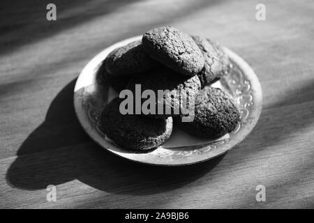 Oatmeal cookies in a silver plate on a wooden table, bw photo. Stock Photo