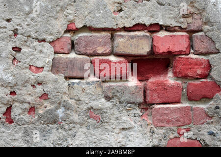 Old ruined wall with sticking out fragments of red bricks and cement Stock Photo
