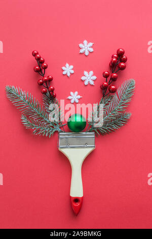 Flat lay of paint brush with christmas tree branches, bauble decoration, snowflakes and red berries minimal creative holiday concept. Stock Photo