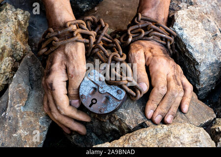 Man's hands are chained. Big old iron castle. Big gray stones. The thin, dirty hands of a slave wrapped in an old rusty chain. Stock Photo