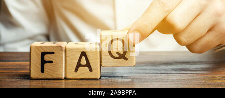 Businessman puts wooden blocks with the word FAQ (frequently asked questions). Collection of frequently asked questions on any topic and answers to th Stock Photo