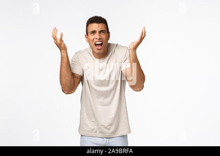 Disappointed and freak-out, bothered handsome man in t-shirt, raising hands up frustrated and displeased, arguing, complaining over unfair failure Stock Photo