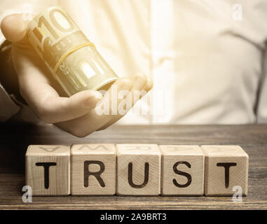 Wooden blocks with the word Trust and money in the hands of a businessman. Trust relationships between business partners, friends, relatives. Respect Stock Photo