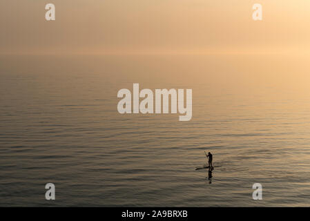 Man practicing stand up paddle boarding on the sea after sunset Stock Photo