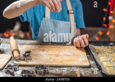 A woman rolls out the dough with a rolling pin and shapes it with her hands for a festive gingerbread on a wooden table background. Christmas mood for Stock Photo