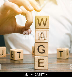 Hand of a businessman removes wooden blocks with the word Wage. Salary reduction concept. Wages cuts. The concept of limited profit. Lack of money and Stock Photo