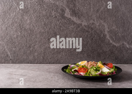 Salad with tuna, egg and vegetables on black plate and gray background. Stock Photo