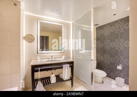 An elegant, modern bathroom with all of the amenities laid out for the guest with lights around the wall and mirror. Stock Photo