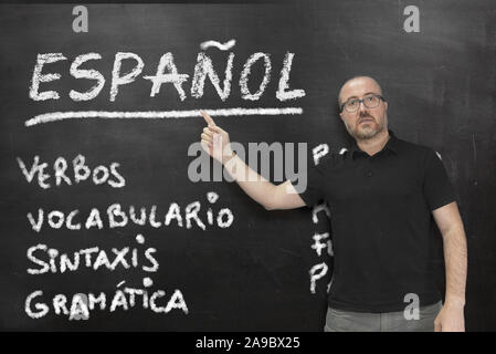 Male Spanish teacher pointing to some language concepts writen on a blackboard in the classroom. Education concept with empty copy space for Editor's Stock Photo