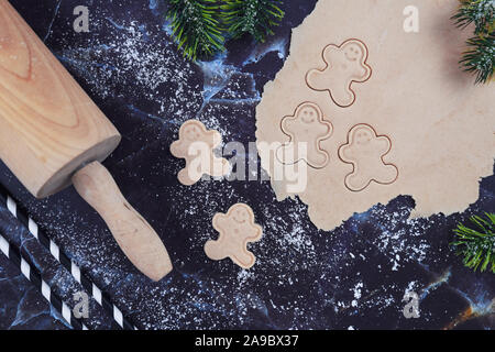 Overhead flat lay concept for baking Christmas cookies with rolled out cookie dough, cookies in the shape of happy gingerbread men, rolling pin Stock Photo
