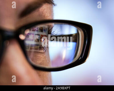 The brown-eyed girl in glasses with a black frame looks at the laptop monitor, close-up