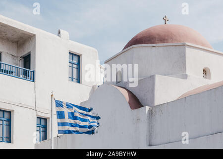 Greek flag in the wind outside the traditional Mykonian church with red top in Mykonos, Greece. Stock Photo