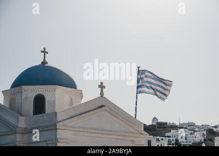 Greek flag in the wind against blur sky, on the orthodox church in Mykonos, Greece. Motion blur. Stock Photo