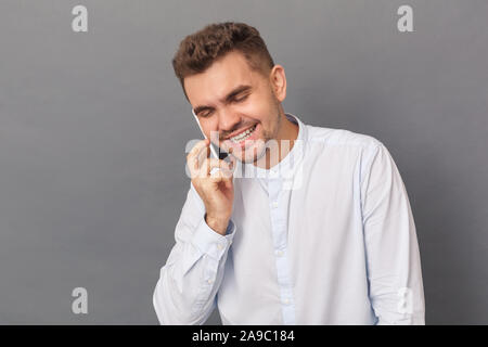 Freestyle. Young man studio standing isolated on grey talking on smartphone laughing cheerful Stock Photo