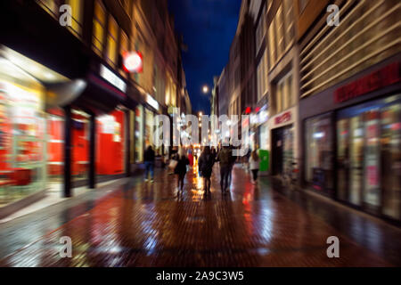 Blurry motion image of young people walking on Kalverstraat street which is one of the main shopping streets in Amsterdam. It is a rainy summer night. Stock Photo