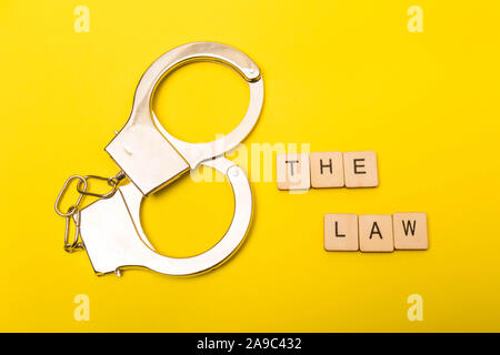 Crime or justice concept showing a sign reading the law on a yellow background with handcuffs Stock Photo