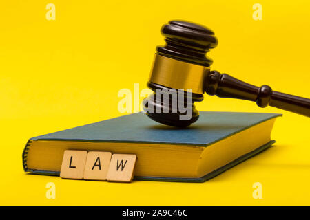 Crime or justice concept showing a gavel on a book with a sign reading law all on a yellow background Stock Photo