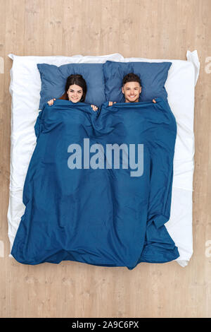 Bedtime. Young couple lying on bed under blanket top view smiling cheerful Stock Photo