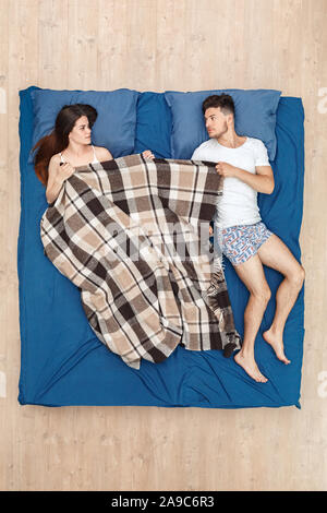 Bedtime. Young couple lying fighting fot blanket on bed top view irritated Stock Photo