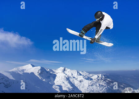Skier Snowboarder jumping through air with blue sky in background Stock Photo